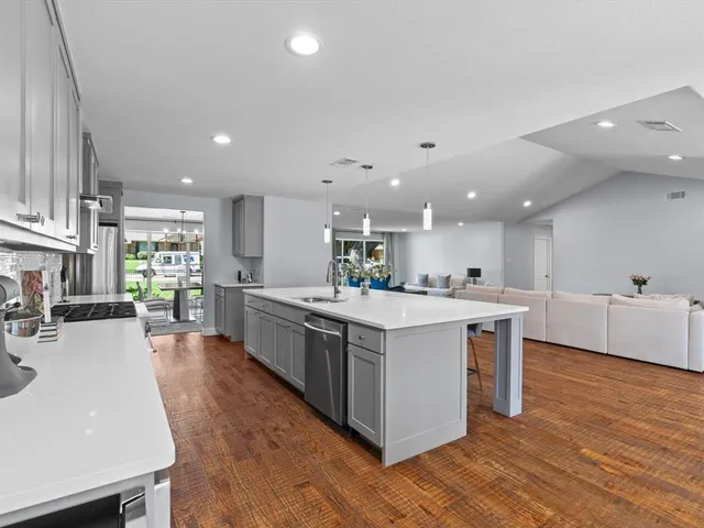 a large kitchen with a large counter top a sink stainless steel appliances and cabinets