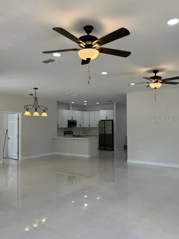an empty room and kitchen view of a ceiling fan