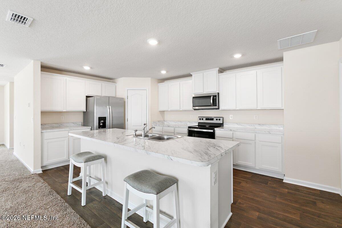 233 Falcon Ridge Road St. Augustine, FL 32084 - Photo 8 of 34 a kitchen with stainless steel appliances granite countertop a refrigerator a stove a sink a microwave and white cabinets with wooden floor