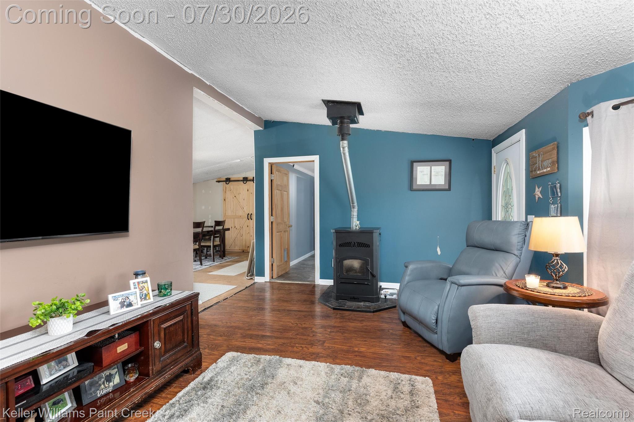 7544 Ravenswood Road Goodells, MI 48027 - Photo 14 of 42 Living area featuring wood-finish flooring, a freestanding stove with exposed vent pipe, and a wall-mounted television