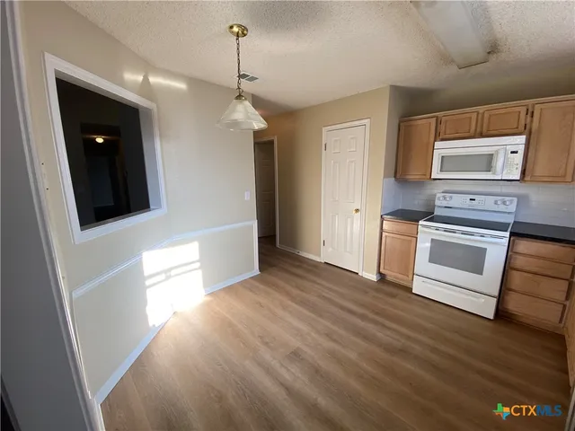 a kitchen with stainless steel appliances granite countertop a refrigerator a sink dishwasher a stove and white countertops with wooden floor