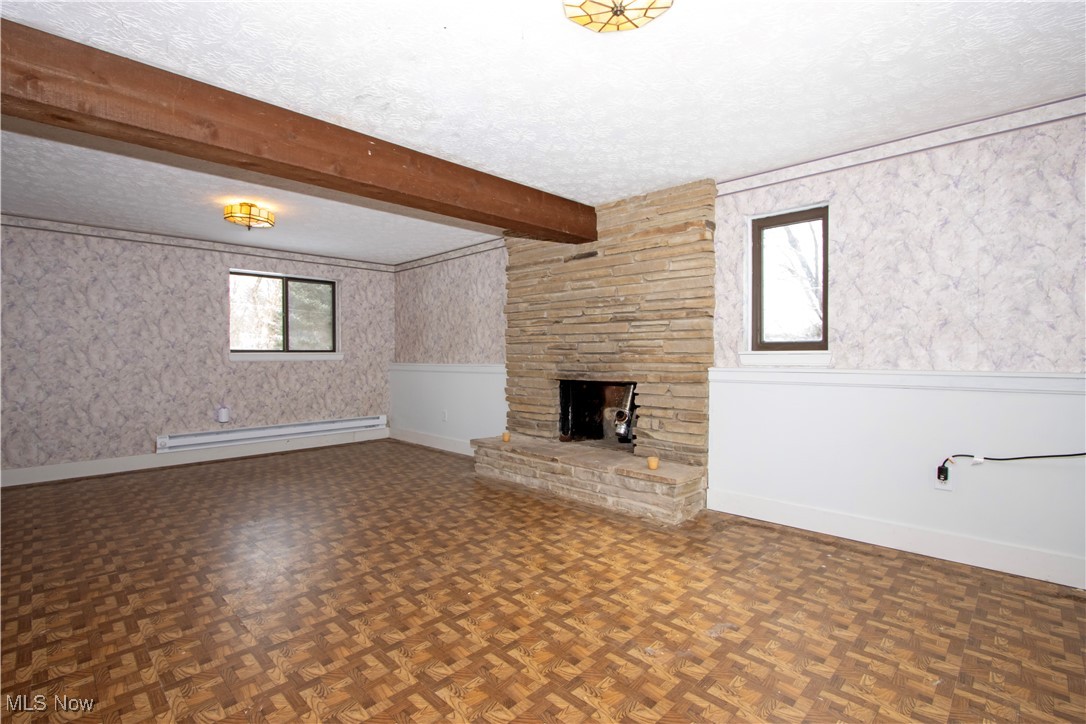 2781 North Firestone Road Wooster, OH 44691 - Photo 8 of 41 Unfurnished living room with dark parquet floors, a fireplace, beamed ceiling, a baseboard radiator, and a textured ceiling