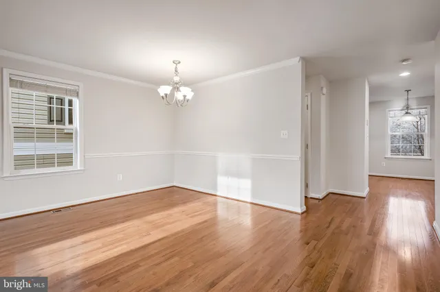 an empty room with wooden floor chandelier and windows