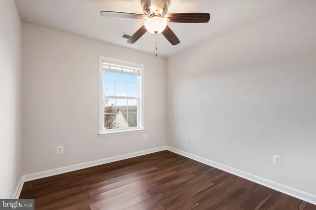 an empty room with wooden floor chandelier fan and windows