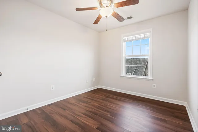 an empty room with wooden floor chandelier fan and windows