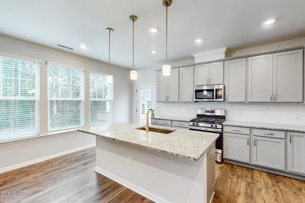 a kitchen with stainless steel appliances granite countertop a stove a sink and white cabinets with wooden floor
