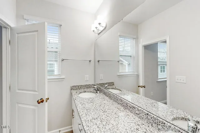 a bathroom with a granite countertop sink a toilet a mirror and window