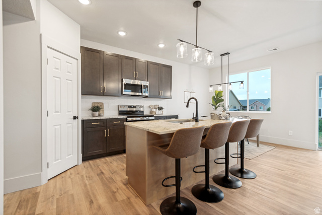 529 North Hvn Drive Mapleton, UT 84664 - Photo 9 of 30 Kitchen featuring dark wood-finish cabinetry, stainless steel appliances, a tile backsplash, and a central island with a light-toned countertop and sink