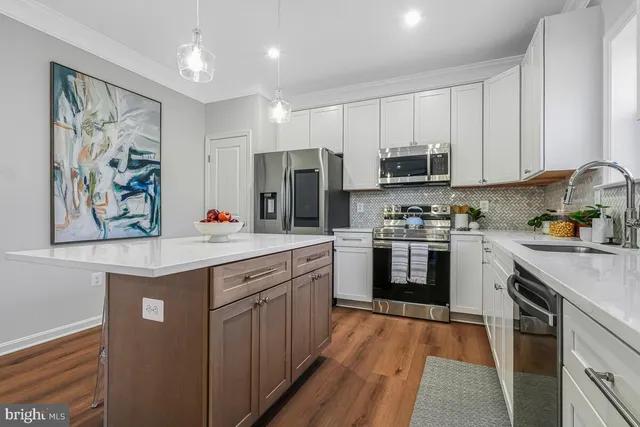 a kitchen with stainless steel appliances granite countertop a stove top oven a sink a refrigerator and white cabinets with wooden floor