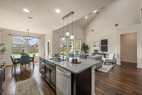 a kitchen with stainless steel appliances granite countertop a stove top oven a sink a dining table and chairs with wooden floor