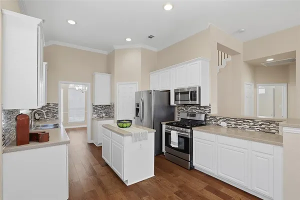 a kitchen with stainless steel appliances a stove top oven a sink a refrigerator white cabinets and wooden floor