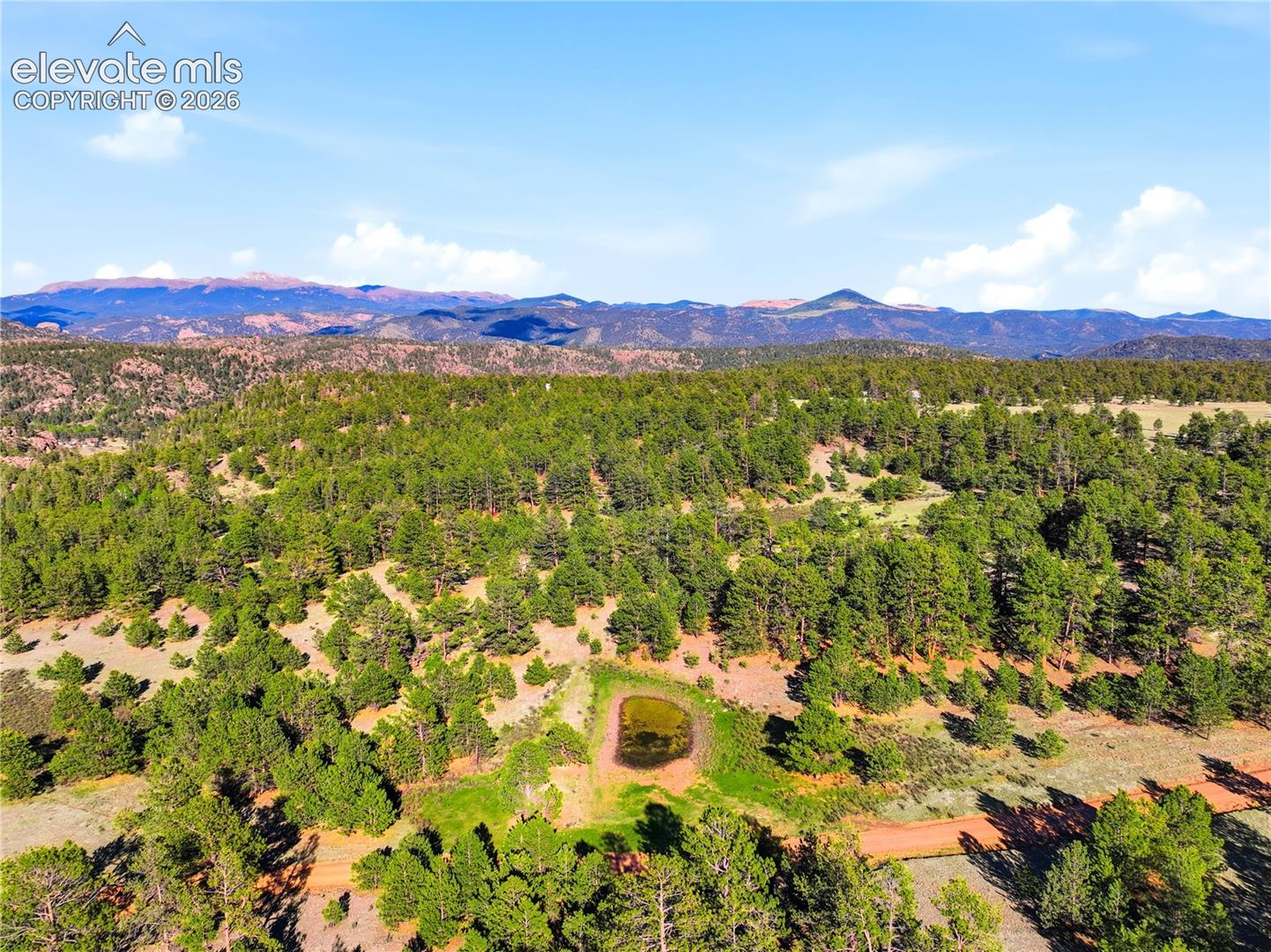 Doe Valley Road Guffey, CO 80820 - Photo 17 of 19 Expansive wooded landscape featuring a natural pond, varied topography, mature evergreen trees, and distant mountain ranges under a clear sky