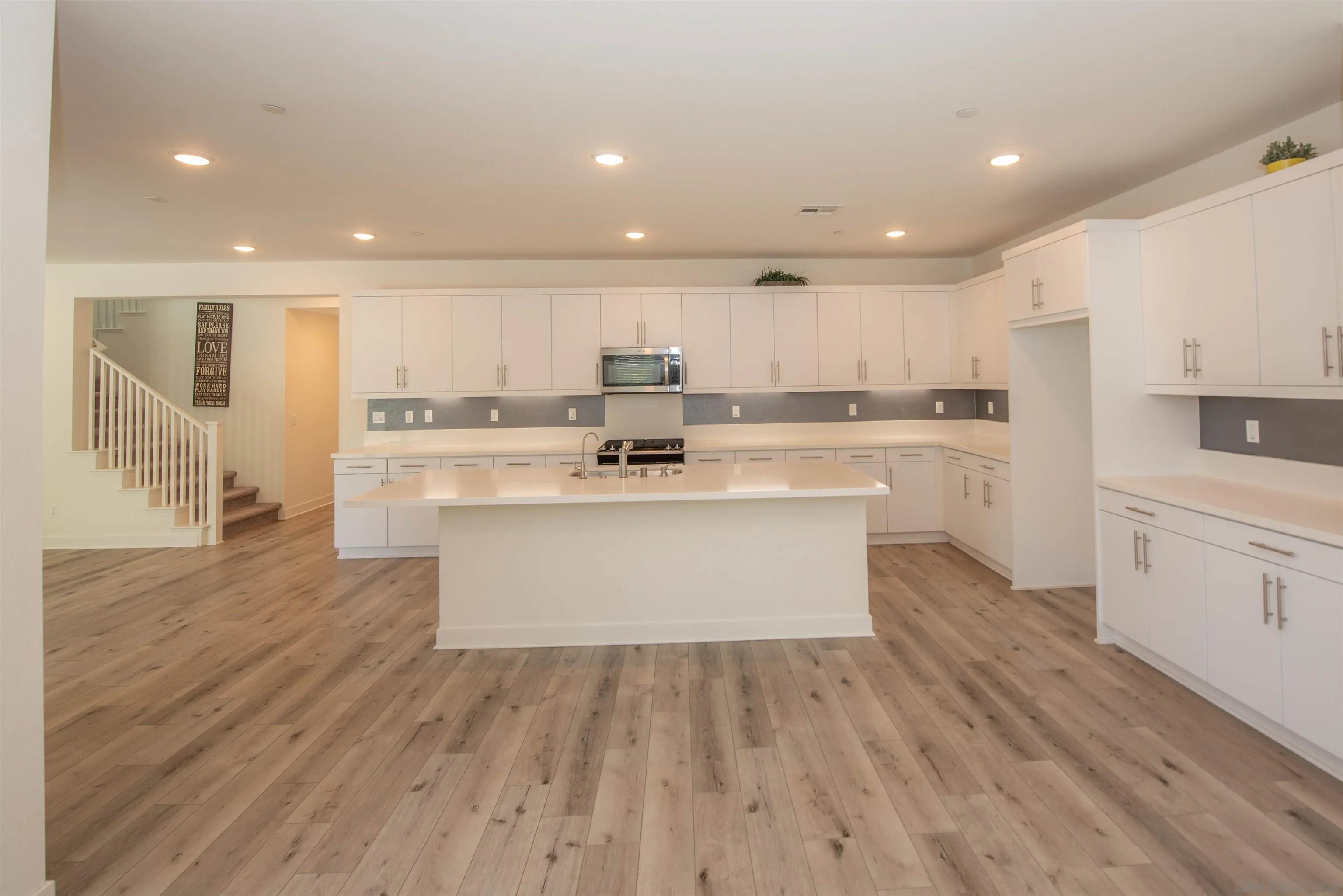 8902 Trailridge Avenue Santee, CA 92071 - Photo 4 of 38 a large kitchen with kitchen island a stove a sink a refrigerator and white cabinets with wooden floor