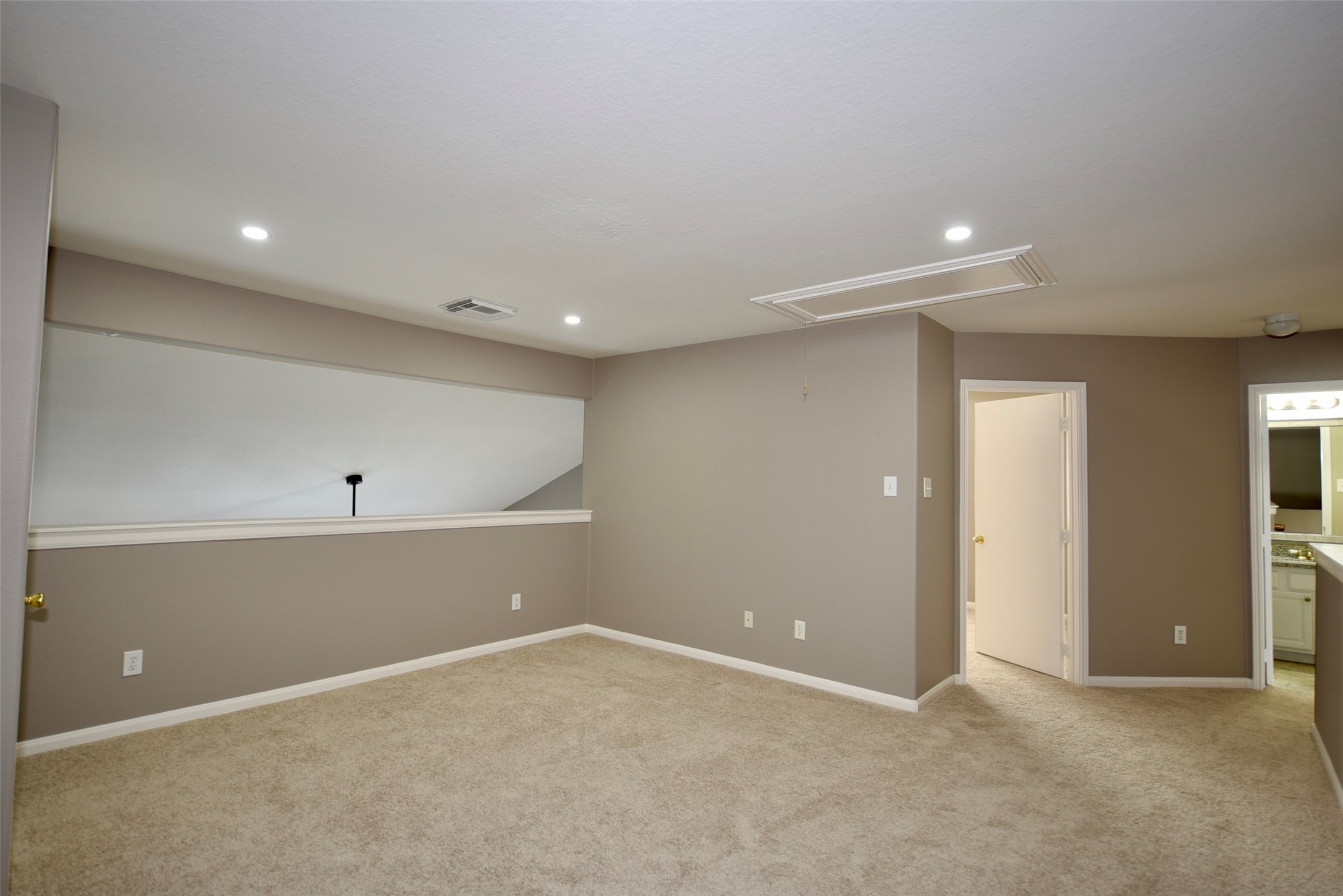 9611 Babbling Spring Court Tomball, TX 77375 - Photo 20 of 31 This photo shows a spacious, carpeted room with neutral walls, recessed lighting, and an open railing overlooking another area. There's access to adjacent rooms, making it versatile for various uses.
