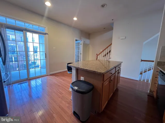 a kitchen with stainless steel appliances granite countertop a refrigerator a stove a kitchen island a dining table and chairs with wooden floor