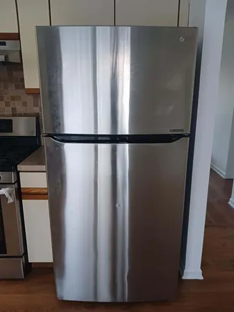 a view of a refrigerator in kitchen and an empty room with wooden floor