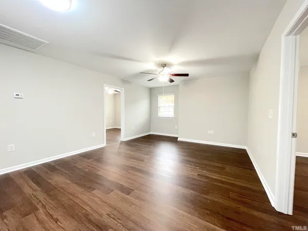 a view of an empty room with wooden floor and a ceiling fan