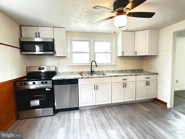 a kitchen with stainless steel appliances white cabinets a sink a stove a microwave and wooden floors