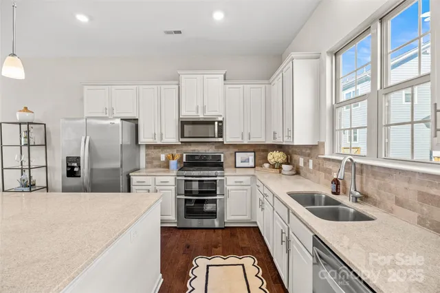 a kitchen with stainless steel appliances granite countertop a stove top oven a sink a refrigerator and white cabinets with wooden floor