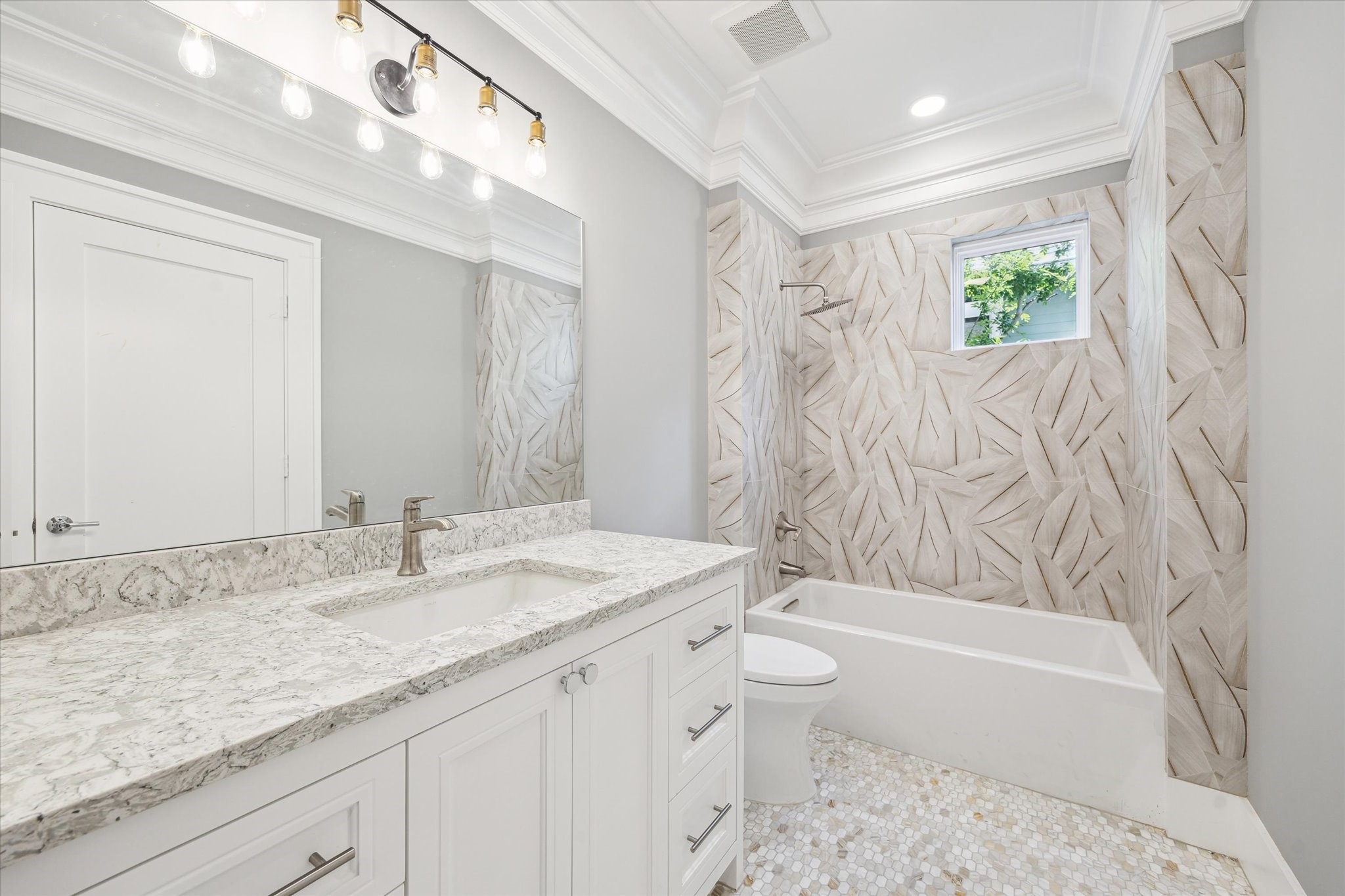 2216 Tangley Street Houston, TX 77005 - Photo 15 of 44 This secondary bathroom features a modern design with a large vanity and marble countertop, a sleek bathtub with decorative tiled walls, and a bright atmosphere enhanced by recessed lighting and a small window.