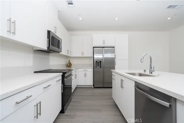 a kitchen with stainless steel appliances a sink dishwasher a refrigerator and a stove with wooden floors