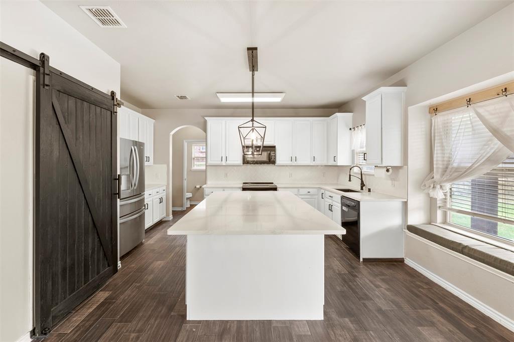 6522 Portside Ridge Lane Dallas, TX 75249 - Photo 9 of 37 Modern kitchen featuring a large central island with a light-toned countertop, white cabinetry, integrated stainless steel appliances, dark wood-finish flooring, and a window seat with a cushion