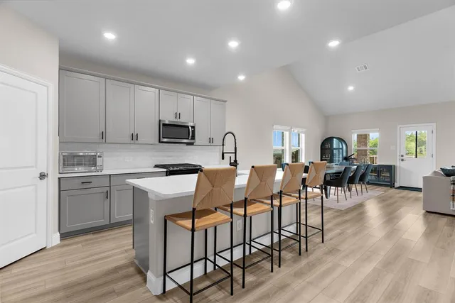 a open kitchen with stainless steel appliances granite countertop a stove a sink a refrigerator a dining table and chairs with wooden floor