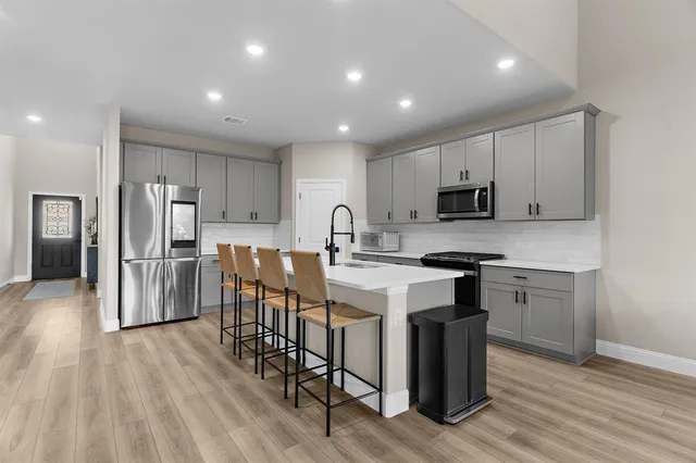 a kitchen with stainless steel appliances a microwave a sink a stove a refrigerator cabinets and wooden floor