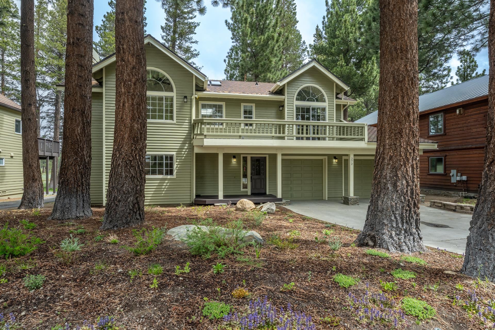 272 Ridge Way Mammoth Lakes, CA 93546 - Photo 4 of 55 Green-hued siding exterior featuring multiple arched windows, an upper-level balcony with a railing, and an attached two-car garage