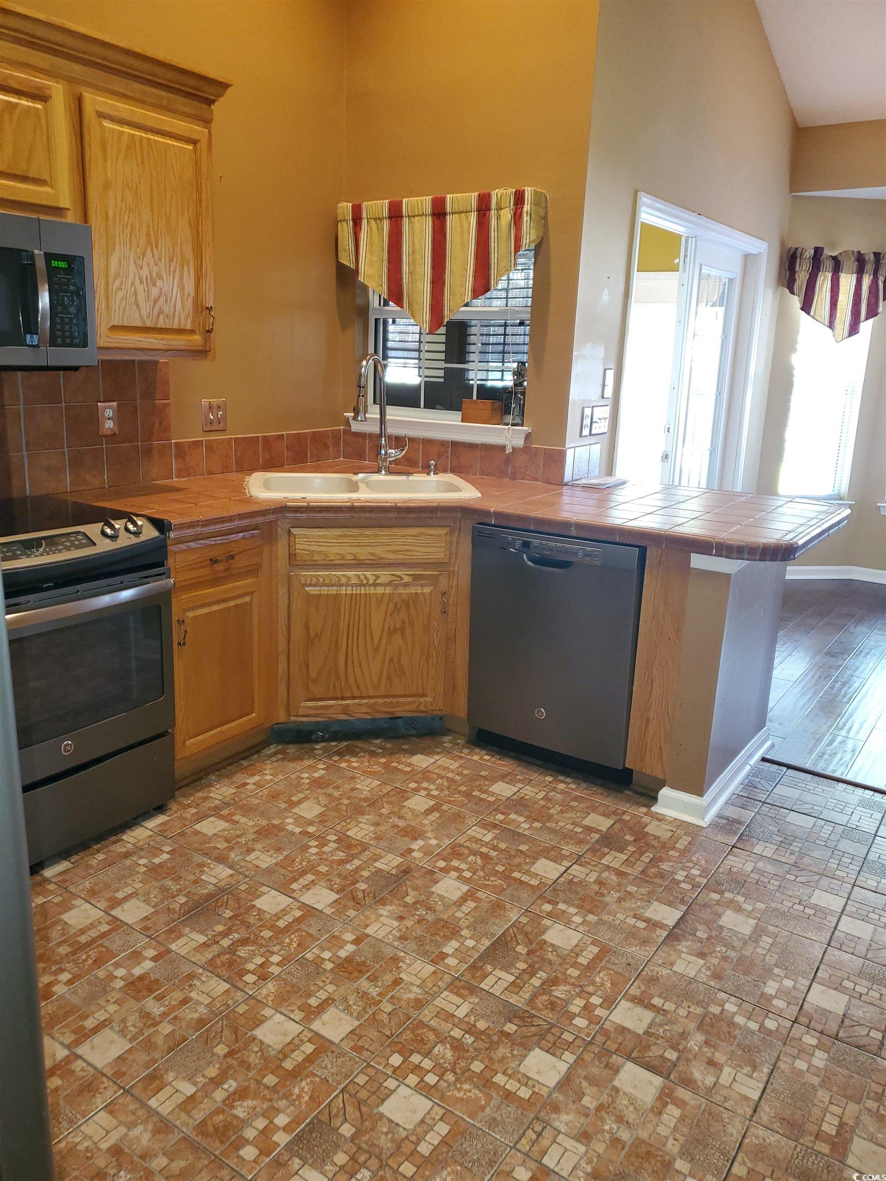 Kitchen featuring a peninsula, stainless steel appliances, tile counters, and decorative backsplash