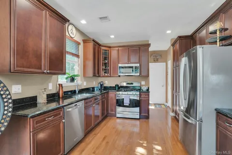 a kitchen with stainless steel appliances kitchen island granite countertop a refrigerator a stove and a sink with wooden floor