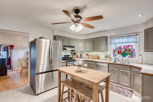 a kitchen with stainless steel appliances a stove a refrigerator a sink a dining table and chairs with wooden floor