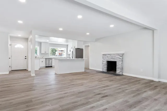 a view of an empty room with wooden floor and a kitchen