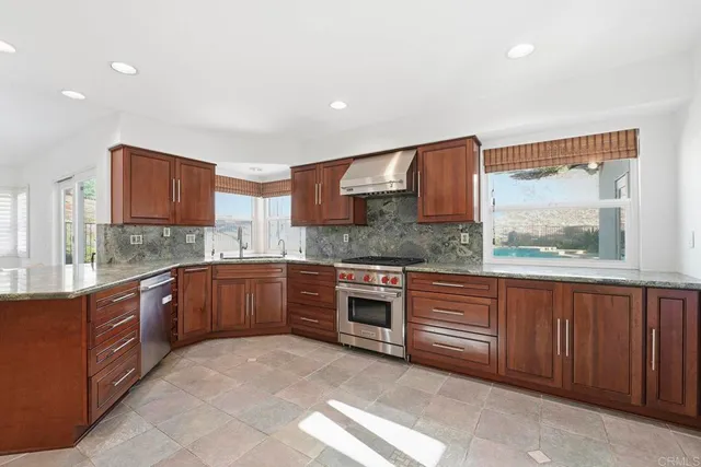 a large kitchen with stainless steel appliances granite countertop wooden cabinets a stove a sink and a large window