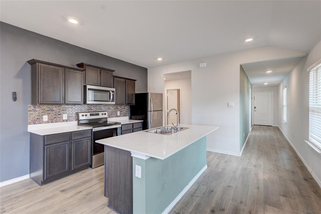 1016 Rio Bravo Drive Forney, TX 75126 - Photo 5 of 25 Kitchen featuring wood-finish flooring, dark wood cabinetry, stainless steel appliances, and a mosaic tile backsplash