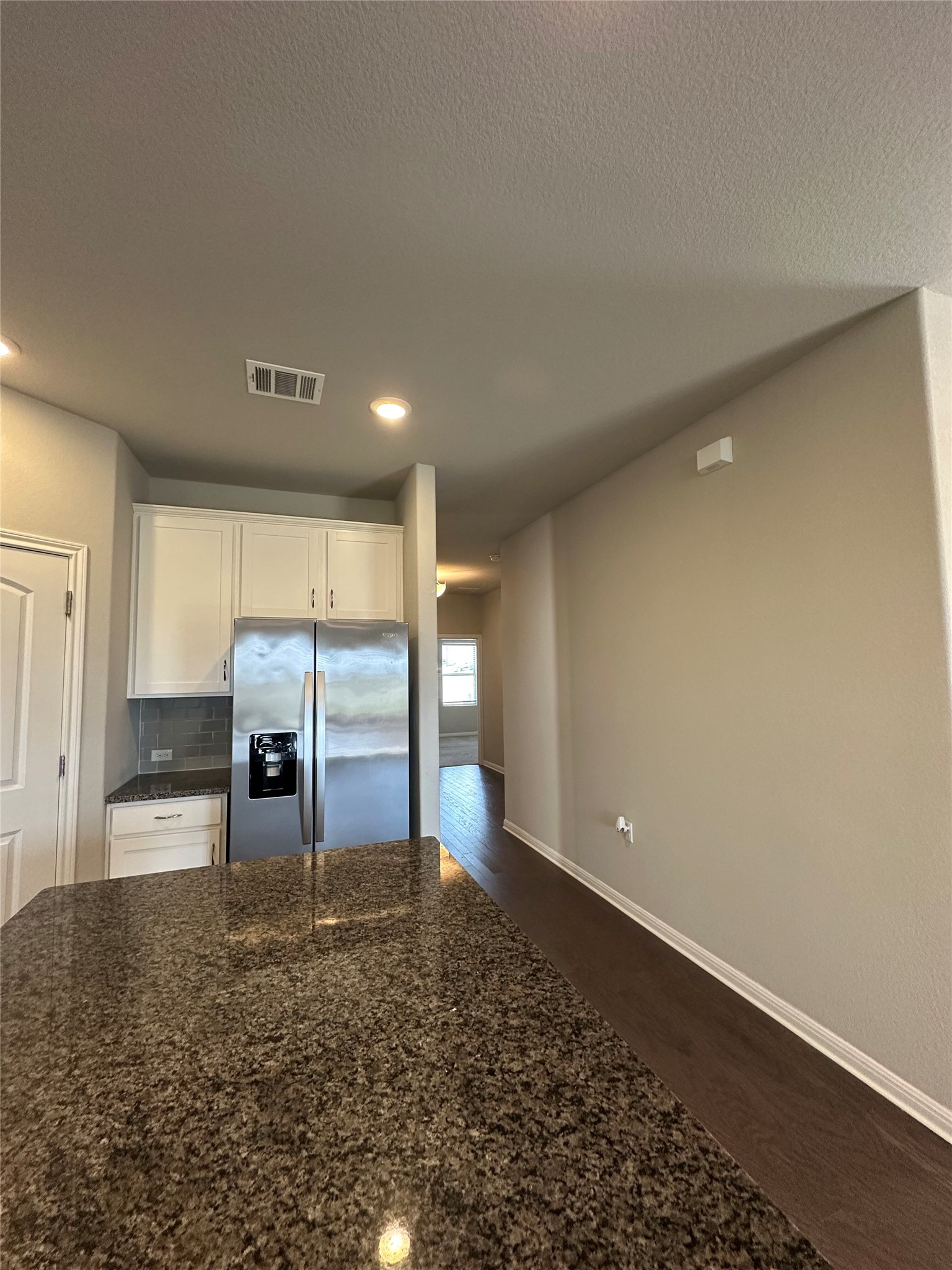 13000 Titanium Street Austin, TX 78754 - Photo 12 of 15 Kitchen featuring stainless steel fridge with ice dispenser, dark wood-type flooring, white cabinets, dark stone countertops, and backsplash
