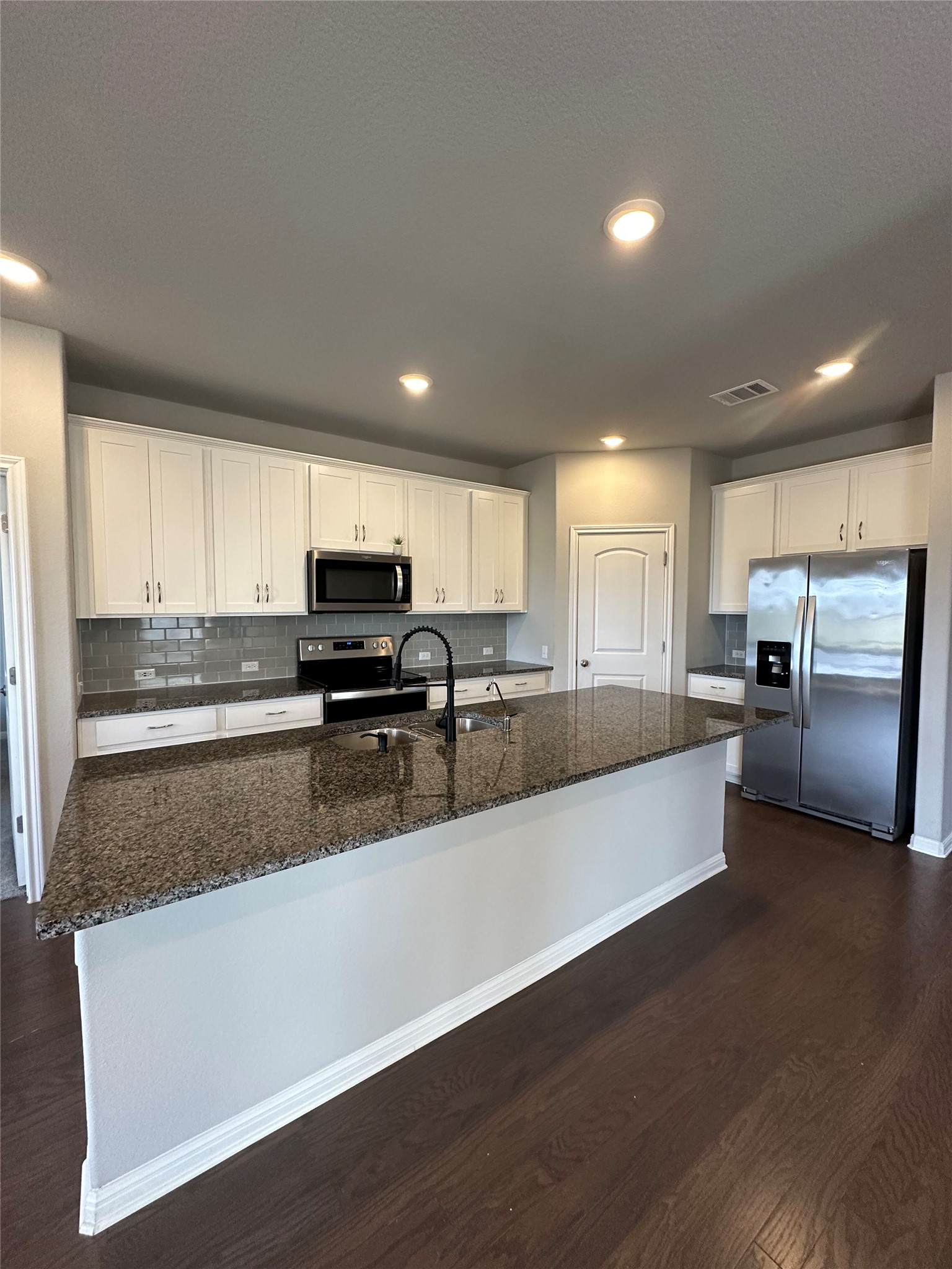 13000 Titanium Street Austin, TX 78754 - Photo 2 of 15 Kitchen featuring stainless steel appliances, white cabinets, dark wood finished floors, dark stone countertops, and a center island with sink