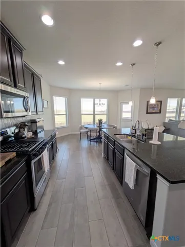 a kitchen with stainless steel appliances granite countertop a stove top oven a sink dishwasher a refrigerator and white cabinets with wooden floor