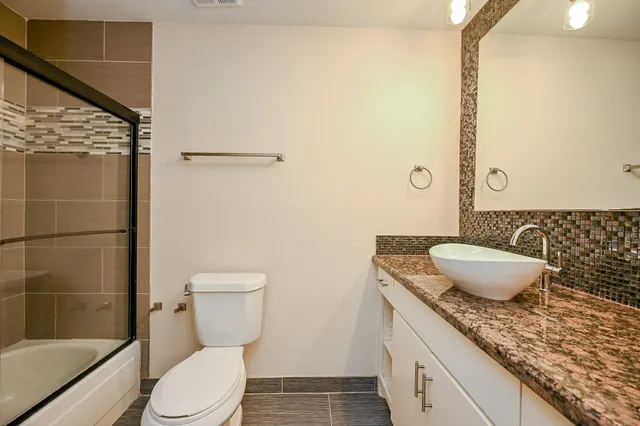a bathroom with a granite countertop sink a toilet a mirror and shower