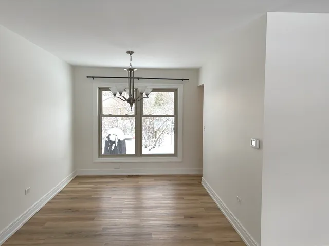 an empty room with wooden floor chandelier and windows