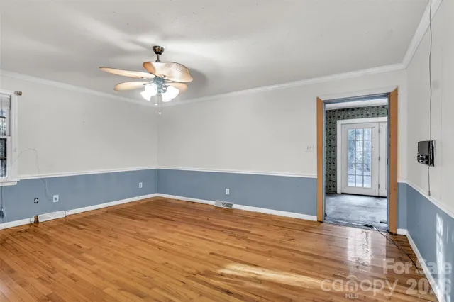 an empty room with wooden floor chandelier fan and windows