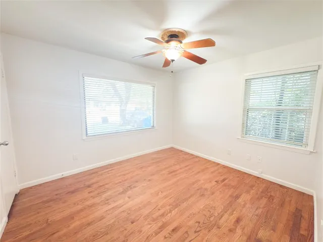 an empty room with wooden floor fan and windows
