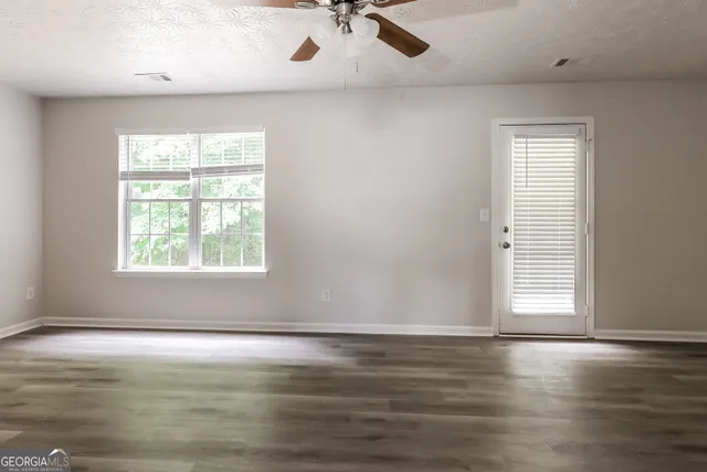 an empty room with wooden floor chandelier fan and windows