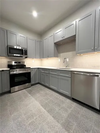 an empty room with wooden floor and way to kitchen