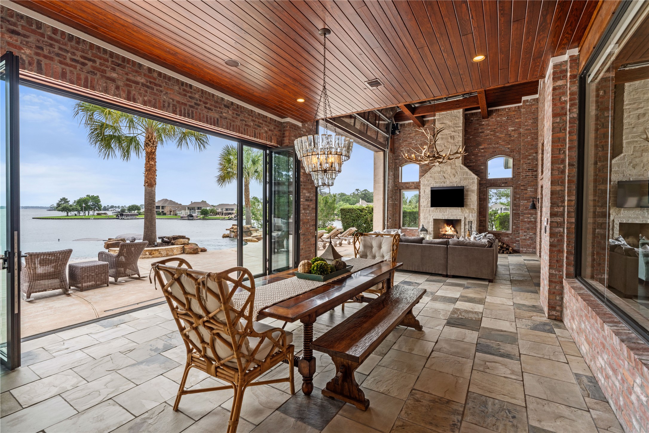 12349 Longmire Trace Conroe, TX 77304 - Photo 35 of 48 Covered lakefront patio with brick fireplace, wood ceiling, and wide glass doors for breezy gatherings.