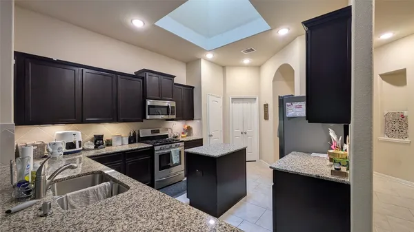 a kitchen with stainless steel appliances kitchen island granite countertop a sink dishwasher stove and refrigerator with wooden cabinets