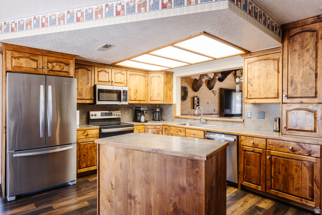 1470 Redwood Tree Street St. George, UT 84790 - Photo 5 of 53 Kitchen featuring wood-finish cabinetry, stainless steel appliances, a center island with a solid surface countertop, and wood-finish flooring
