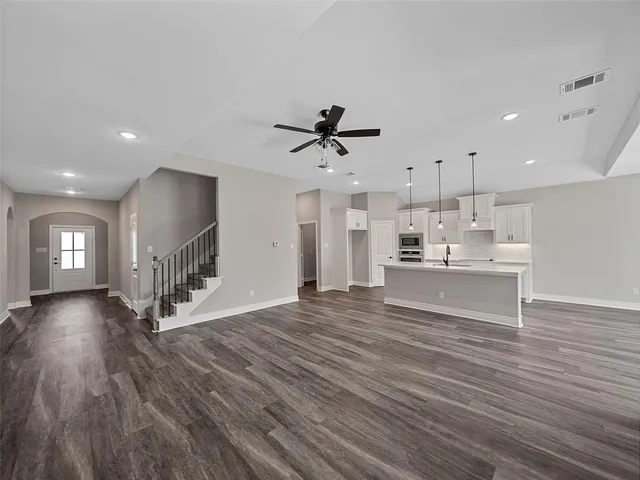 a view of an empty room and kitchen view with wooden floor