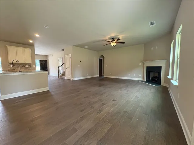 an empty room with wooden floor fireplace and kitchen view