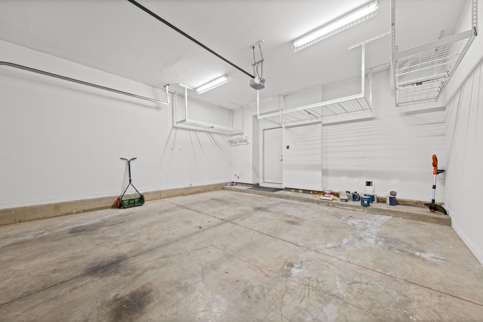 448 Tennessee Street Memphis, TN 38103 - Photo 10 of 39 Spacious garage featuring a concrete floor, bright overhead lighting, two built-in overhead storage racks, a wall-mounted slat storage system, and a side access door